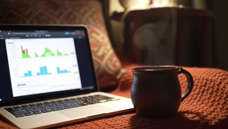 a cozy workspace featuring a laptop displaying data analytics next to a steaming mug on a textured blanket in a warm, inviting setting