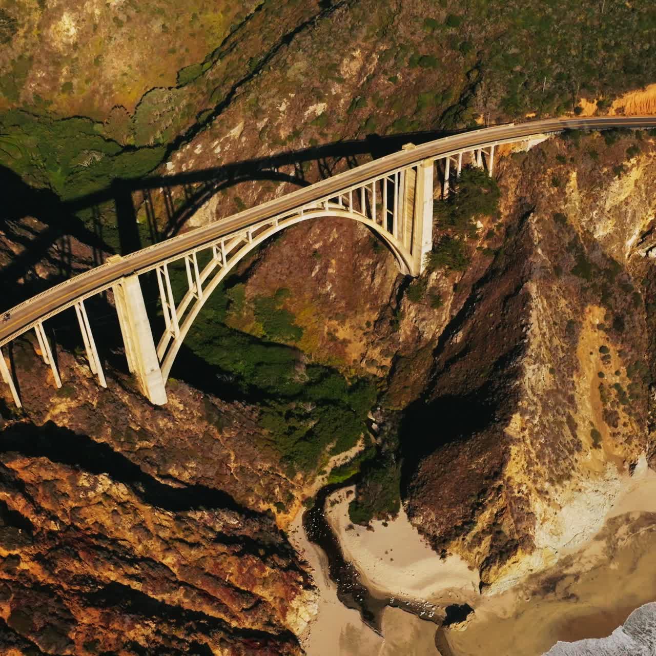 Sunlit rocks of the California coastline. Beautiful arched bridge connecting the mountains and highways on them. Aerial view