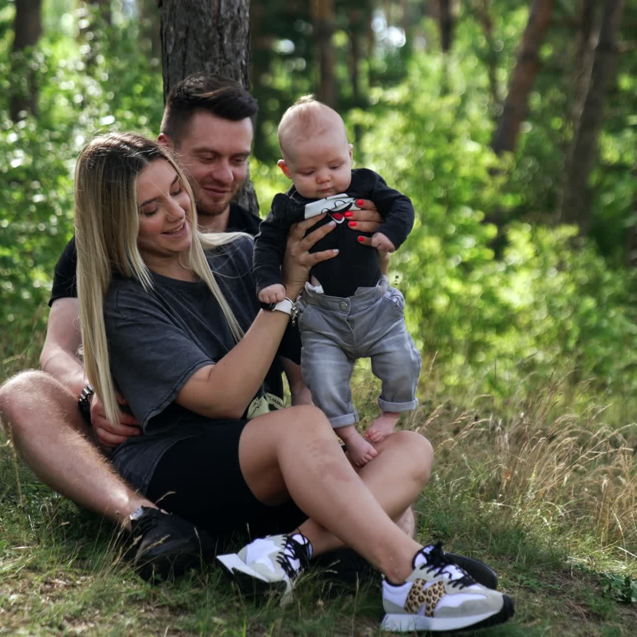 Coppia di sportivi seduta vicino all'albero con il loro neonato in braccio. Una felice famiglia di tre persone trascorre del tempo nella natura