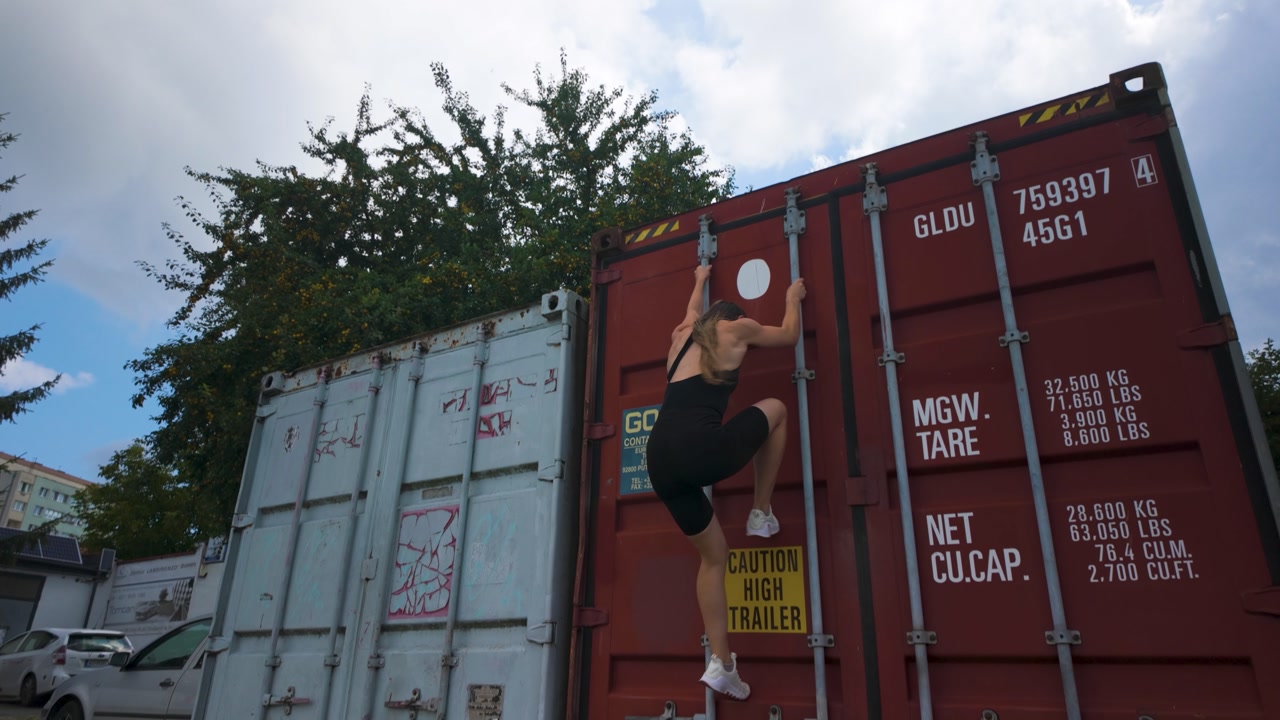 Skilled girl climbing down a big red street container. Tilt down