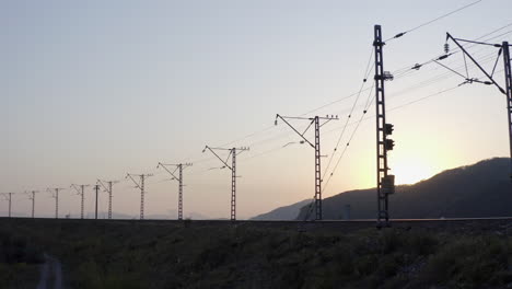 一條空的鐵路,有高電壓電線,日落時,太陽躲在山後面