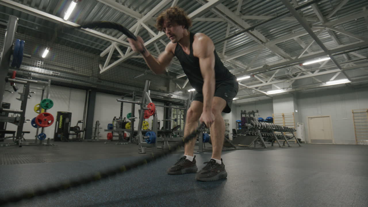 Athletic Man Exercising with Battle Ropes in Gym