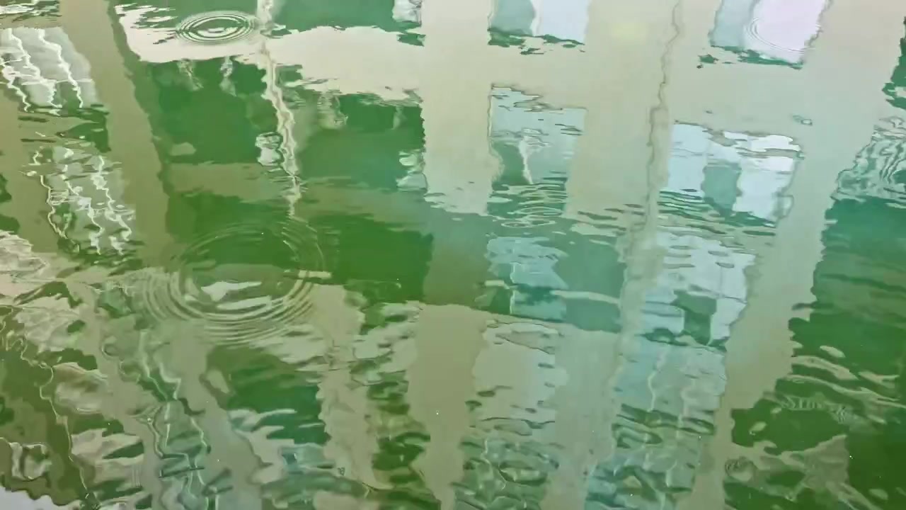 昼間の都市で、水面に建物が反射し、太陽光が水面に模様を描いています。