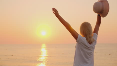 una mujer con un sombrero en la mano se encuentra emocionalmente con el amanecer sobre el mar