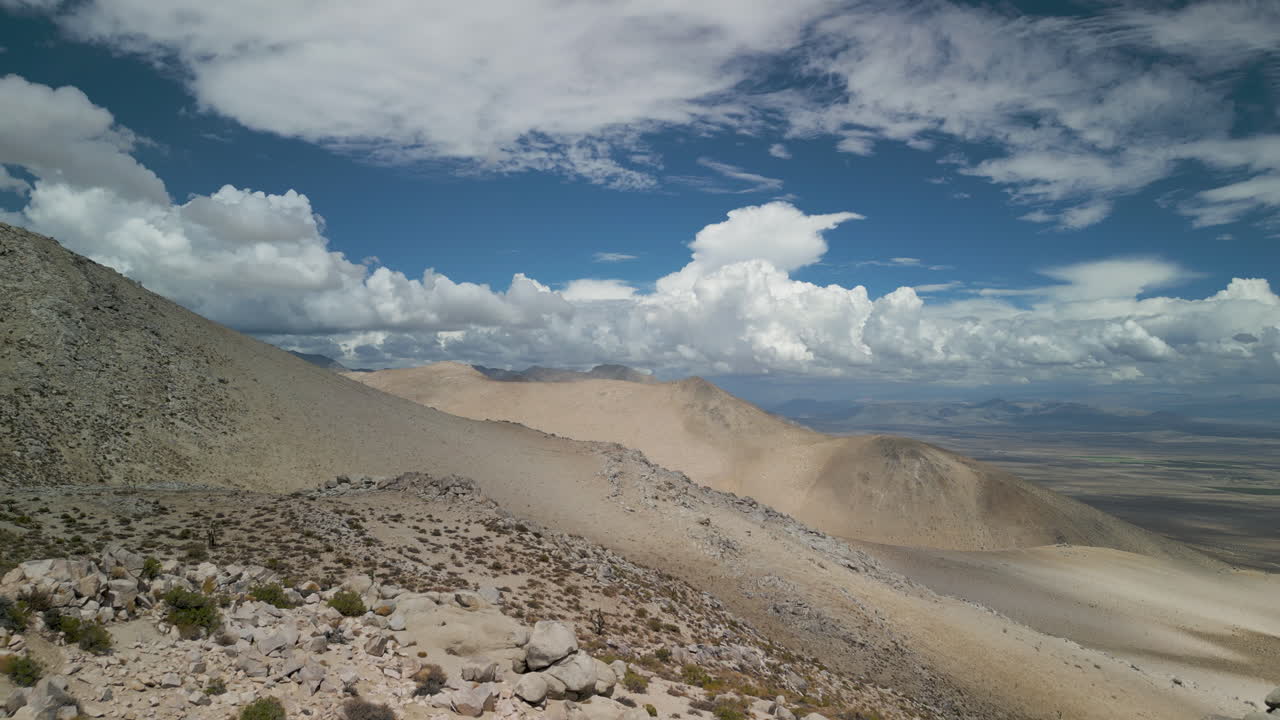 A drone crests over a sandy trail ridgeline to reveal a greater desert view