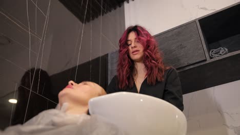 blonde woman sitting on the chair getting hair washed in hair salon by stylist. blonde woman sitting on the chair getting hair washed in hair salon by stylist. high quality footage