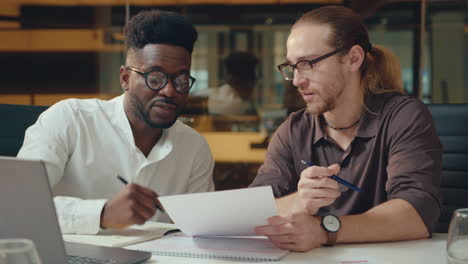 male coworkers discussing document and business plan on laptop