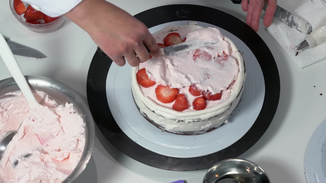 크림으로 인 케이크의 을 조심스럽게 만지기 위해 아이싱 스파라를 사용하는 베이커의 앞.