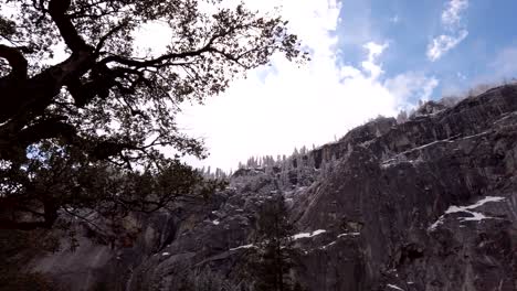 Slow-rotating-upward-shot-of-the-tree-lined-cliff-tops-of-Yosemite-Park-against-Blue-sky-and-fluffy-white-clouds