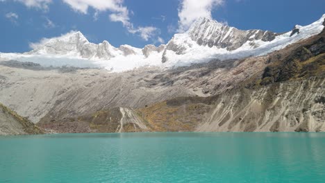 a stunning aerial tilt up shot of turquoise glacial lake beneath the majestic, snow-covered cordillera blanca mountains along peru’s iconic santa cruz trek
