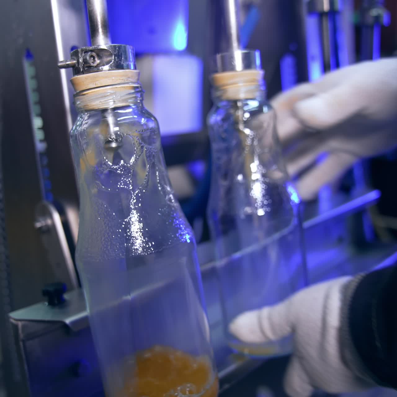 Glass bottles being filled with freshly-squeezed apple juice. Close up. Automated system for manufacturing organic food