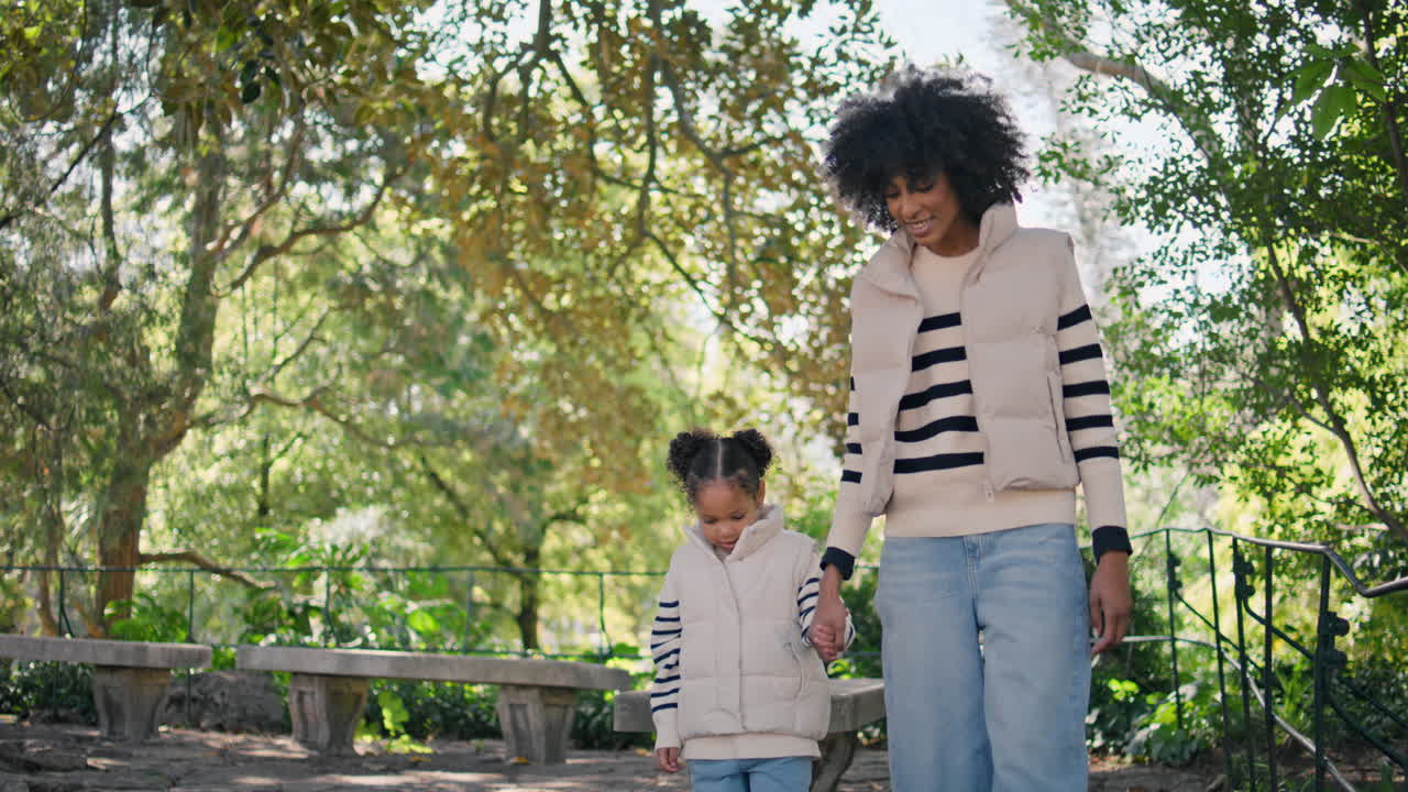 Mother leading little daughter by hand walking green park. Girl holding mom hand