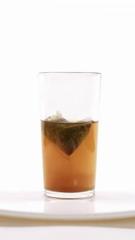 infusión de té en curso con una bolsa de té sumergida en agua caliente en un vaso transparente en un plato