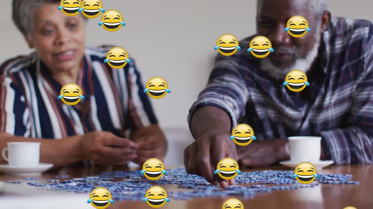Multiple face emojis floating against african american senior couple smiling while playing puzzle