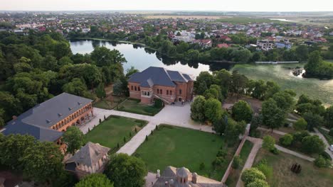 The-historic-mogoșoaia-palace-in-romania,-surrounded-by-greenery-and-water-at-dusk,-aerial-view