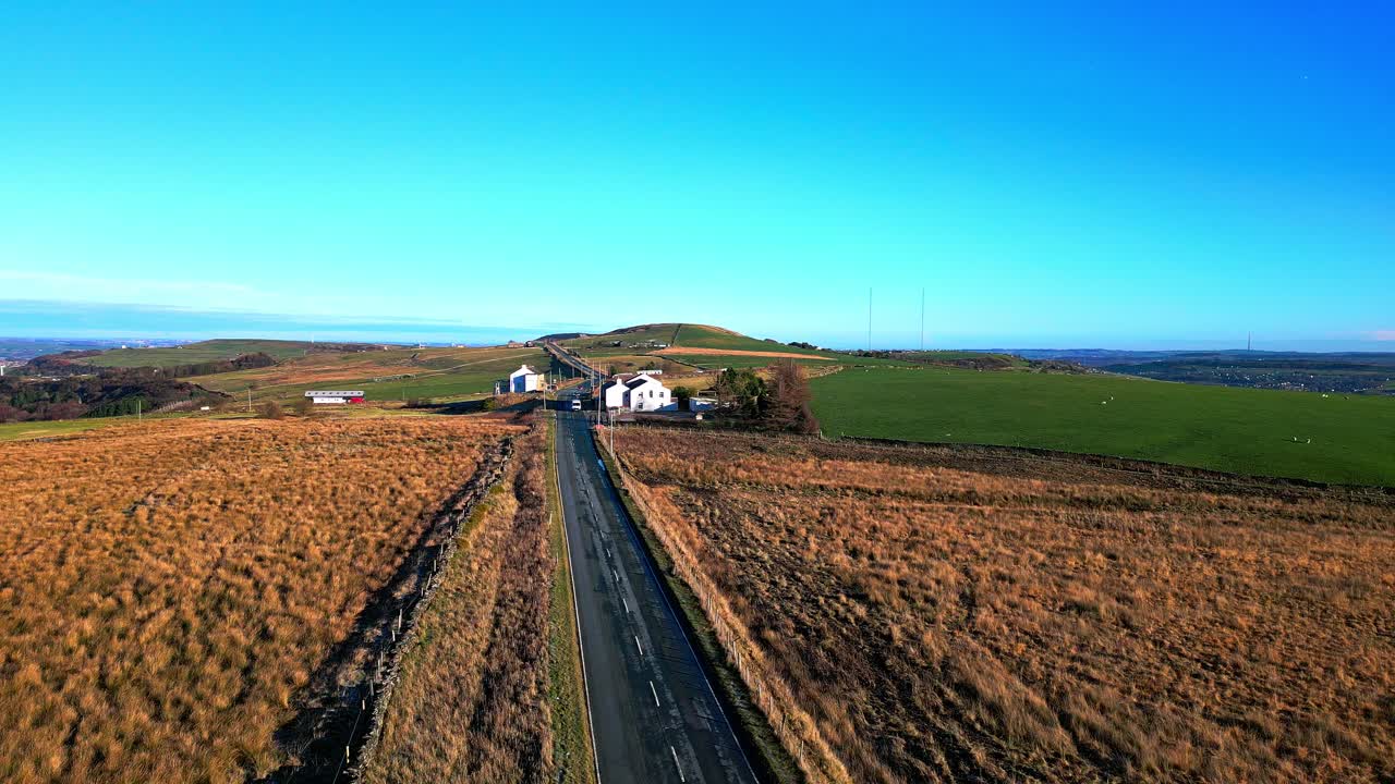 imágenes de video de un dron aéreo de un automóvil, una camioneta conduciendo por una carretera rural y pasando por edificios encalados, en lo alto de las colinas pennine, reino unido