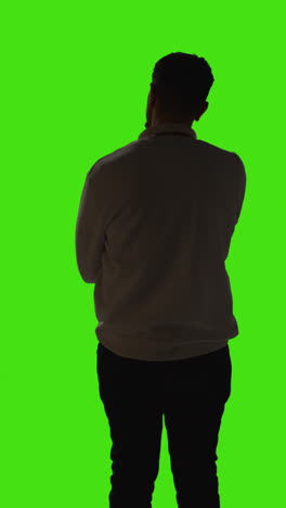 Vertical-Video-Silhouetted-Rear-View-Shot-Of-Man-Standing-And-Waiting-Against-Green-Screen-With-Low-Key-Lighting