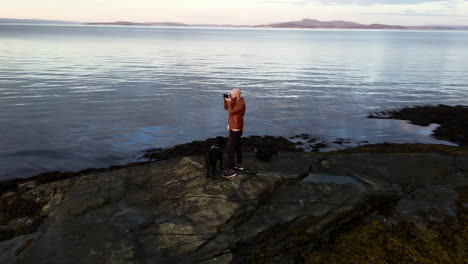 Aerial-footage-of-a-man-standing-at-the-shore-and-taking-pictures-with-a-camera