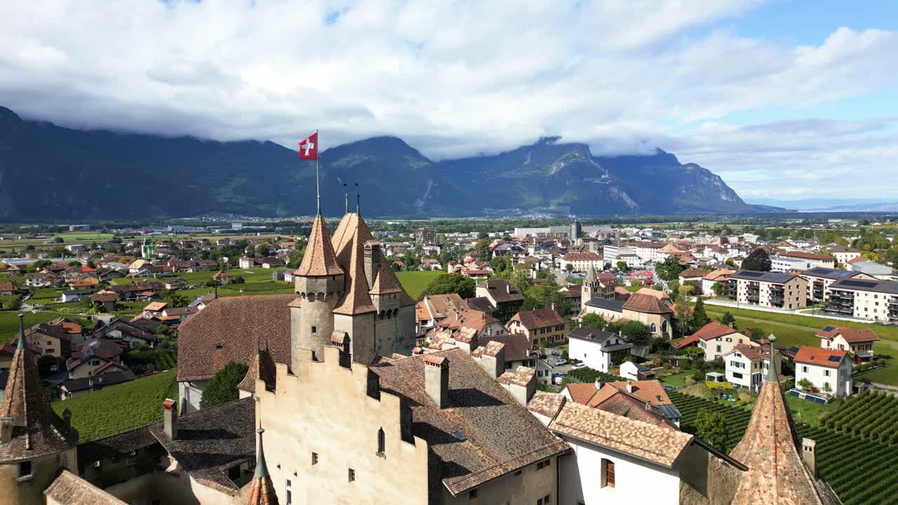 Dolly out drone shot above magnificent Aigle Castle in Vaud Switzerland with Swiss flag waving