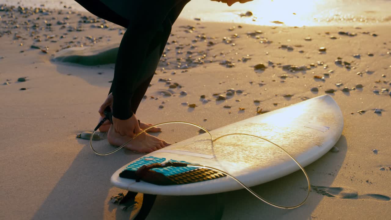 vista lateral de un surfista caucásico adulto atando la correa de la tabla de surf en la playa 4k