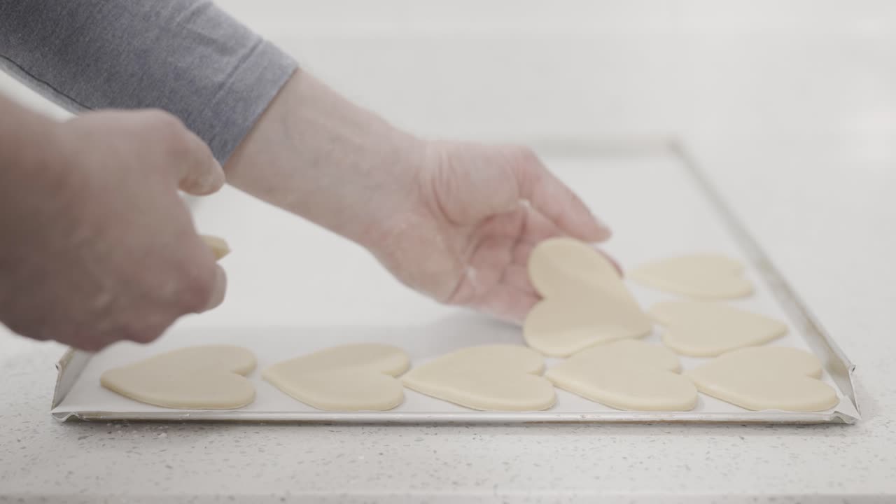 Medium shot of putting freshly rolled out heart-shaped cookies on a baking tray before putting into the oven at a pastry shop, 4K slow motion