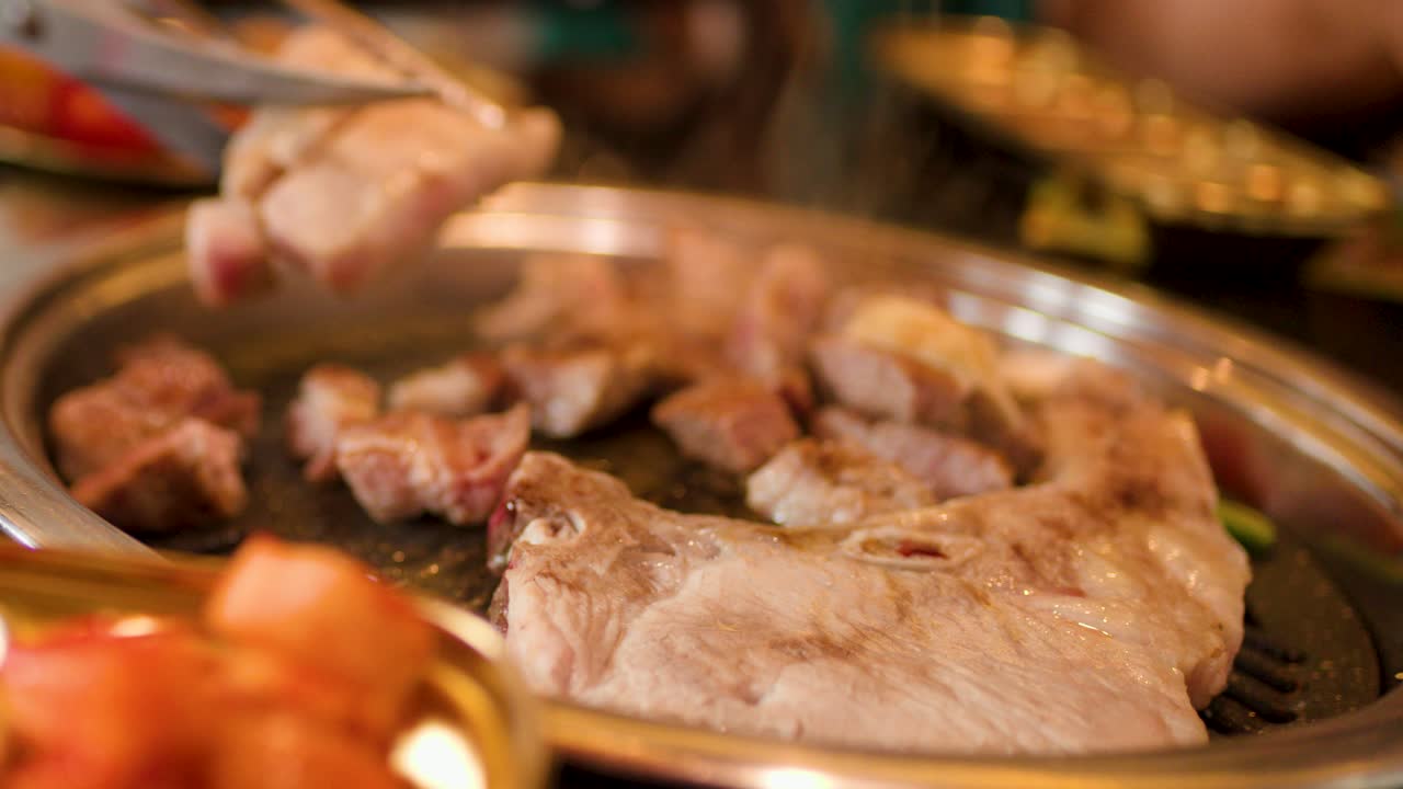 Slices of beef and lamb cook on a round grill, warm lighting, shallow depth of field