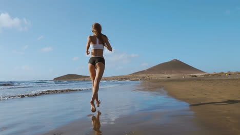 beautiful sportive woman running along beautiful sandy beach, healthy lifestyle, enjoying active summer vacation near the sea. slow motion steadicam.