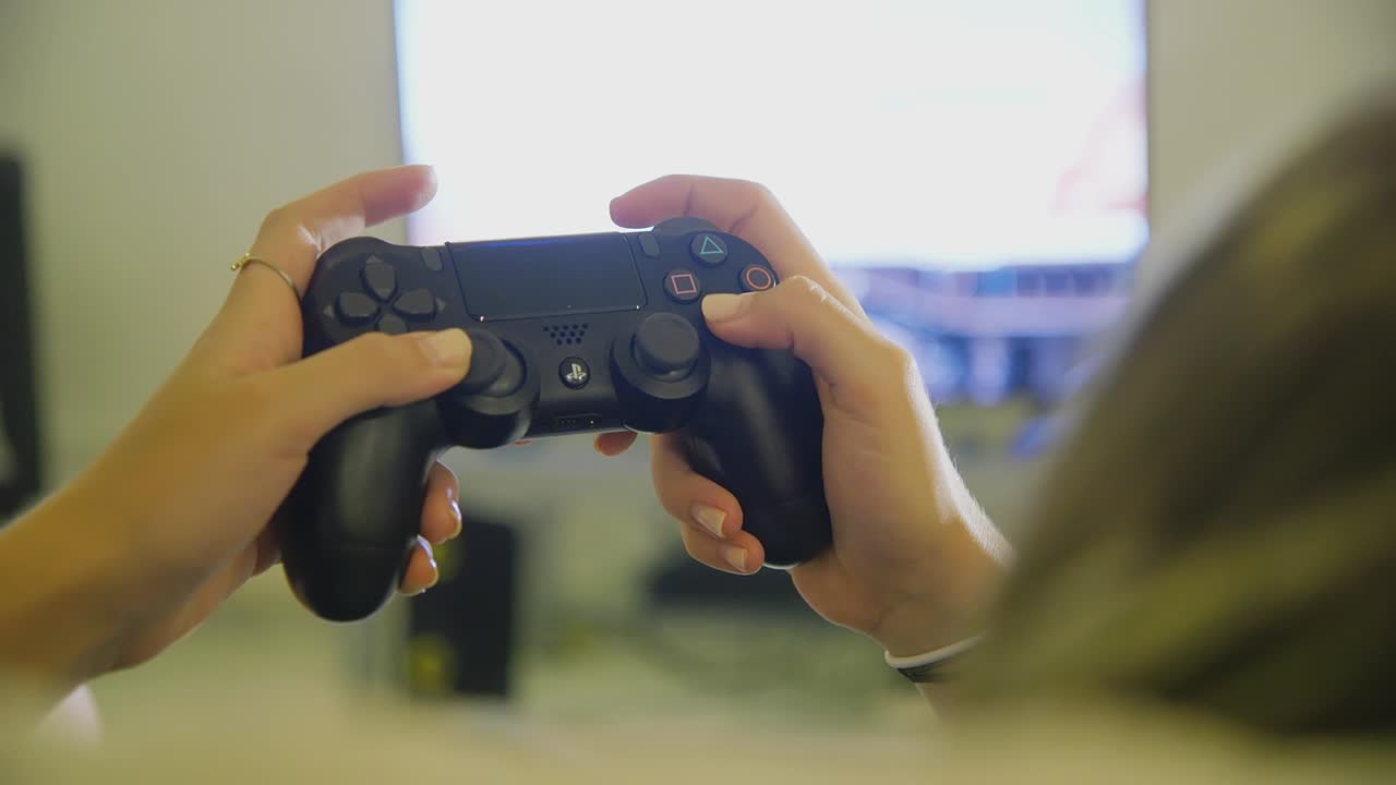 kvinnliga händer som använder svart ps4 dualshock-kontroll för att spela spel inomhus med tv i bakgrunden