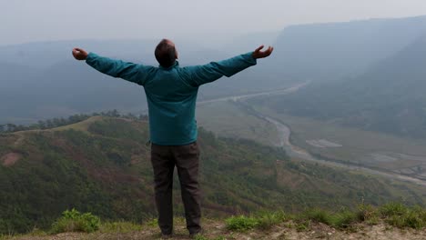 Mann,-Der-Die-Natur-Auf-Einem-Hügel-Mit-Nebligem-Bergwuthintergrund-Aus-Einem-Flachen-Winkelvideo-Genießt,-Wird-In-Nongjrong-Meghalaya,-Indien,-Aufgenommen