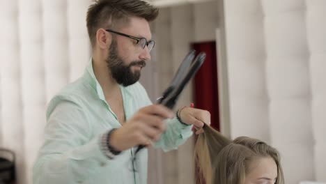 un peluquero profesional enderezando el cabello de una mujer en una peluquería