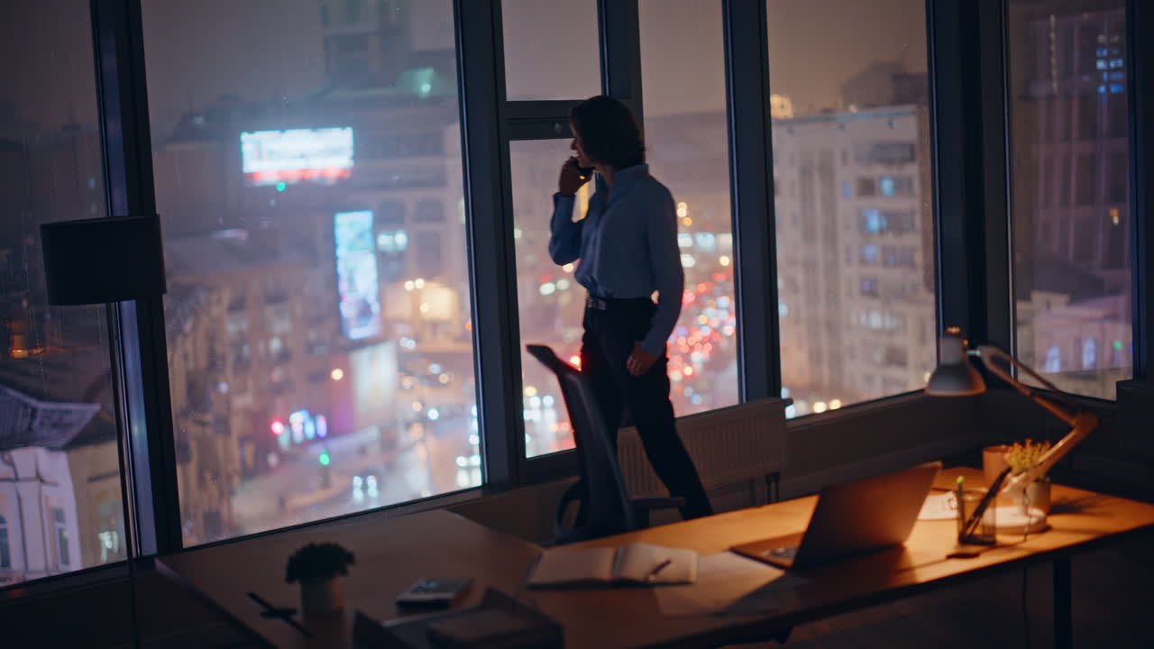 Silhouette businesswoman talking cellphone by office window with night city view