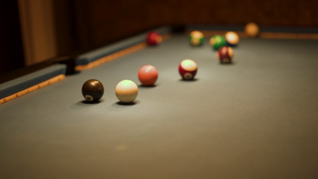Multiple billiard balls roll on green felt table, warm indoor lighting, shallow depth of field