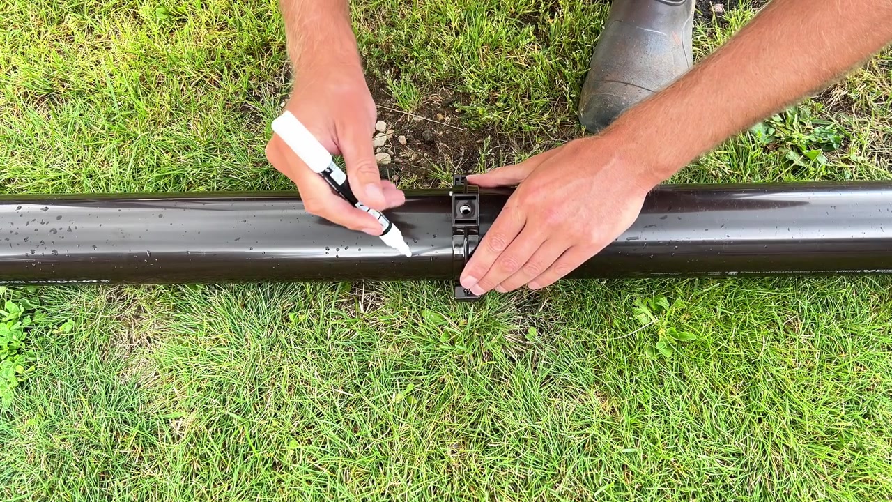 A person uses a white marker to draw a cutting line along a plastic gutter downspout pipe outdoors. Perfect for DIY construction, plumbing guides, and home repair videos.