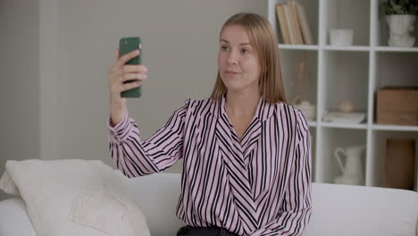 young woman is filming training video by camera of smartphone sitting at home taking selfies