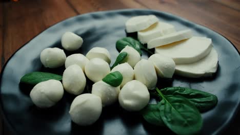 white small mozzarella cheese balls, spinach leaves on black plate. dolly-in shot