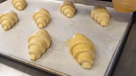 a baker painting egg wash on to croissants that will be baked in a cafe