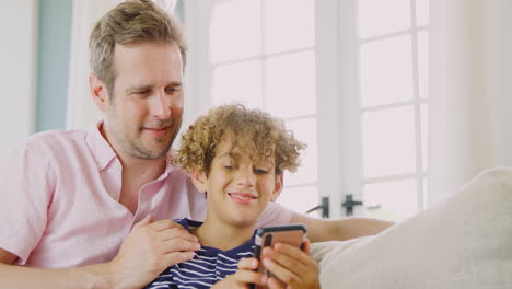 Vater-Und-Sohn-Sitzen-Zu-Hause-Auf-Dem-Sofa-Und-Spielen-Gemeinsam-Ein-Videospiel-Auf-Dem-Handy