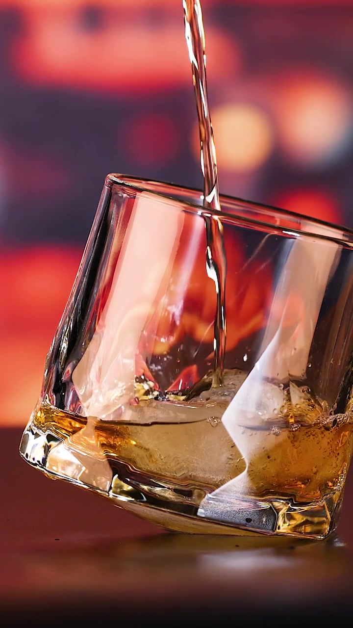 Whiskey dorato versato in un bicchiere tumbler con ghiaccio