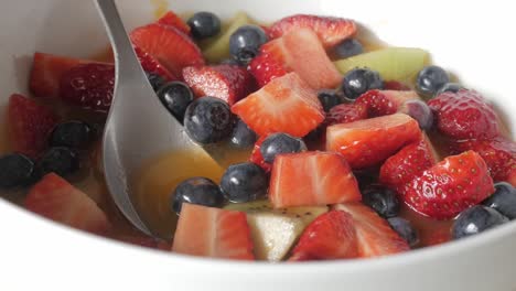 tight zoom in on a vibrant fruit salad mix including strawberries, blueberries, kiwi and sauce in white bowl