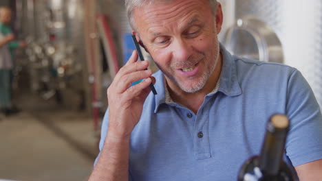 mature man on mobile phone with laptop checking production inside winery