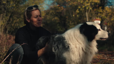 woman smiles as she pets dog in field on autumn day