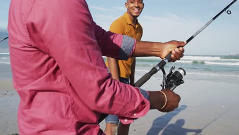 african american senior father and twin teenage sons standing on a beach fishing and talking