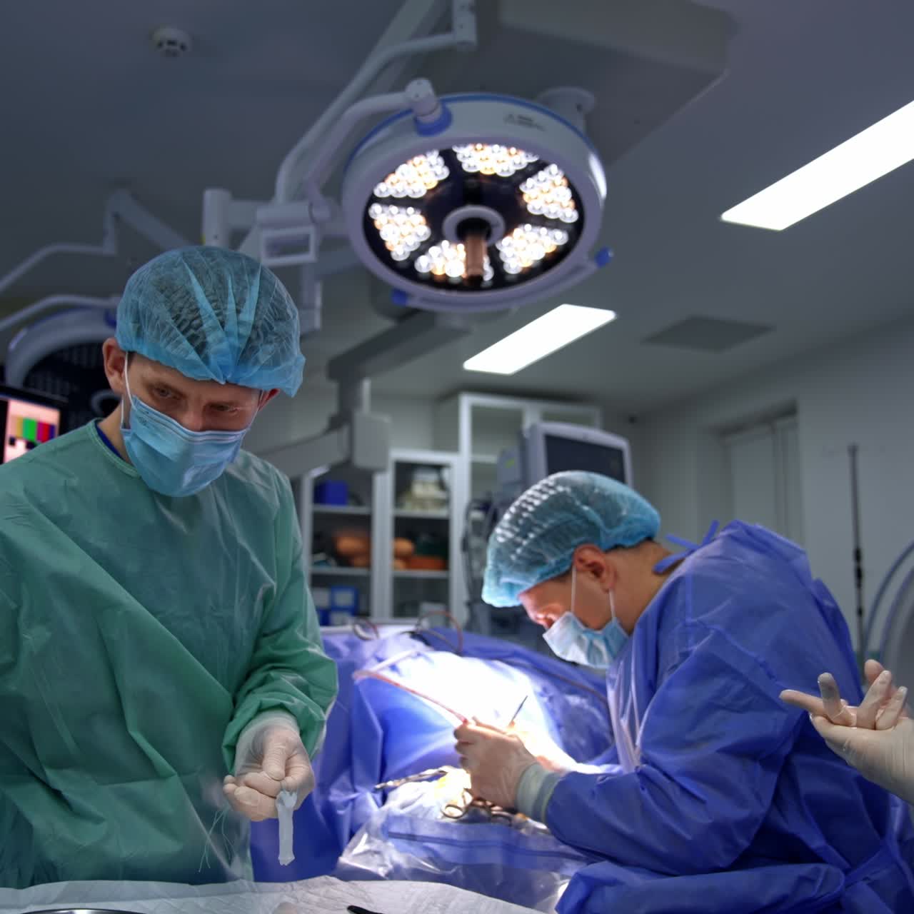 Two medics assisting the neurosurgeon at operation. Male assistant passing the forceps to the main doctor. Advanced equipment at backdrop