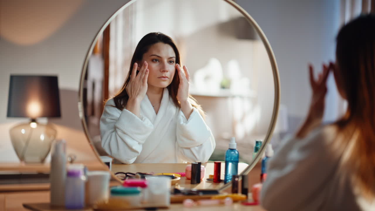 Woman looking mirror reflection sitting bedroom in white robe at morning closeup