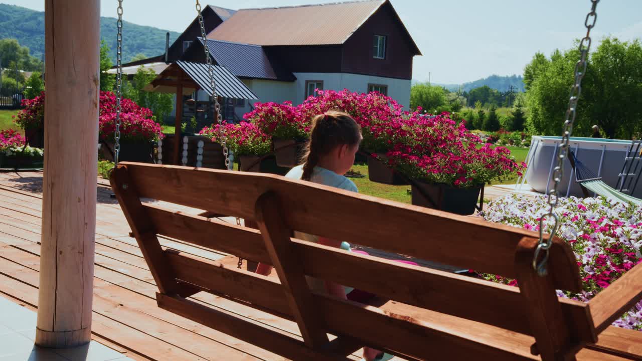 Ragazza che dondola su un'altalena di legno in un bellissimo giardino estivo