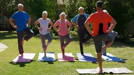 rear view of caucasian male trainer training senior people in performing yoga at the garden of n 4k