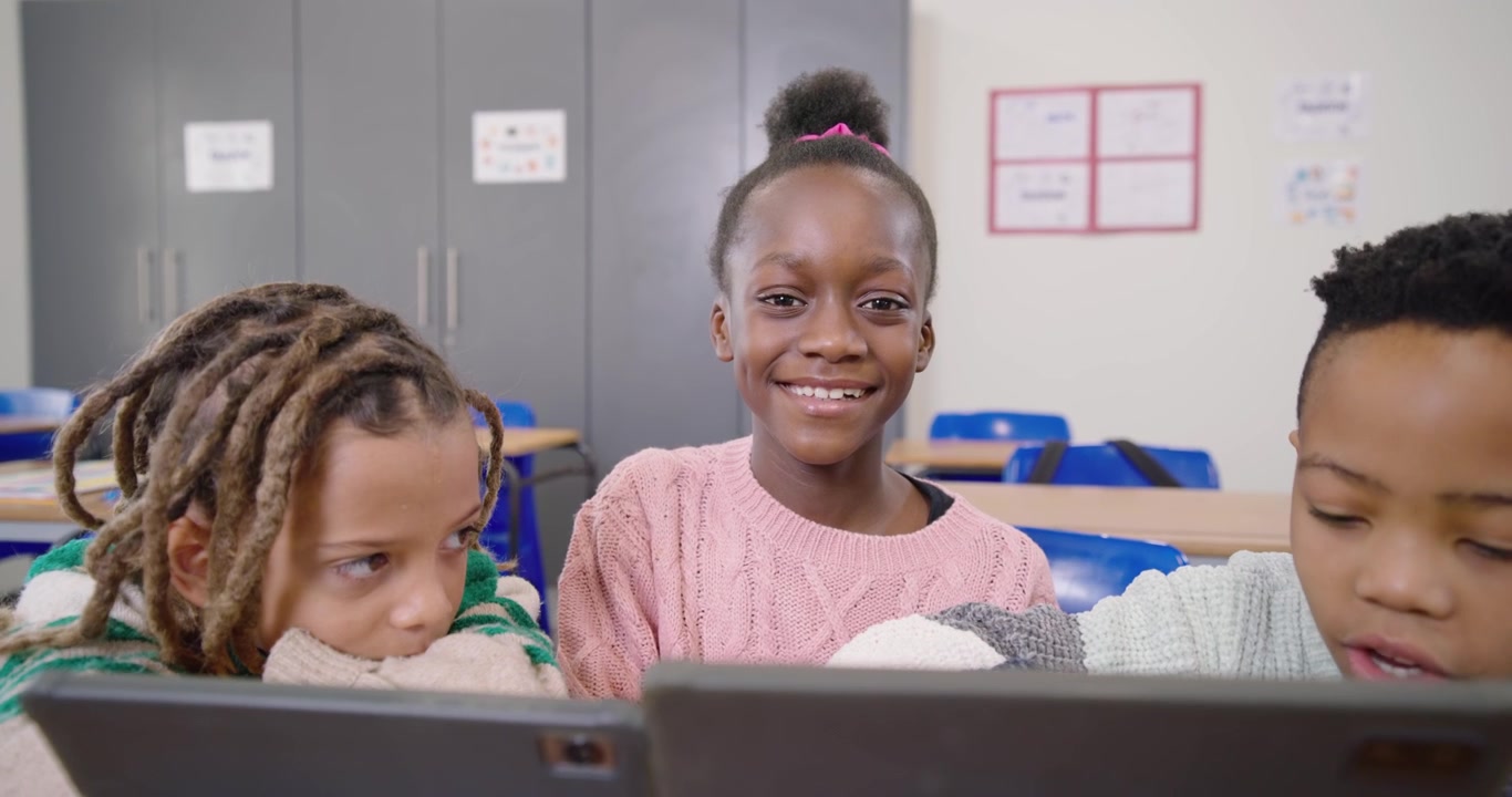 Bambini afroamericani guidati dai tablet che si sporgono, toccando gli schermi in classe, sorridendo.
