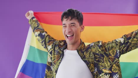 retrato de un feliz hombre biracial sosteniendo una bandera lgbt con los brazos abiertos