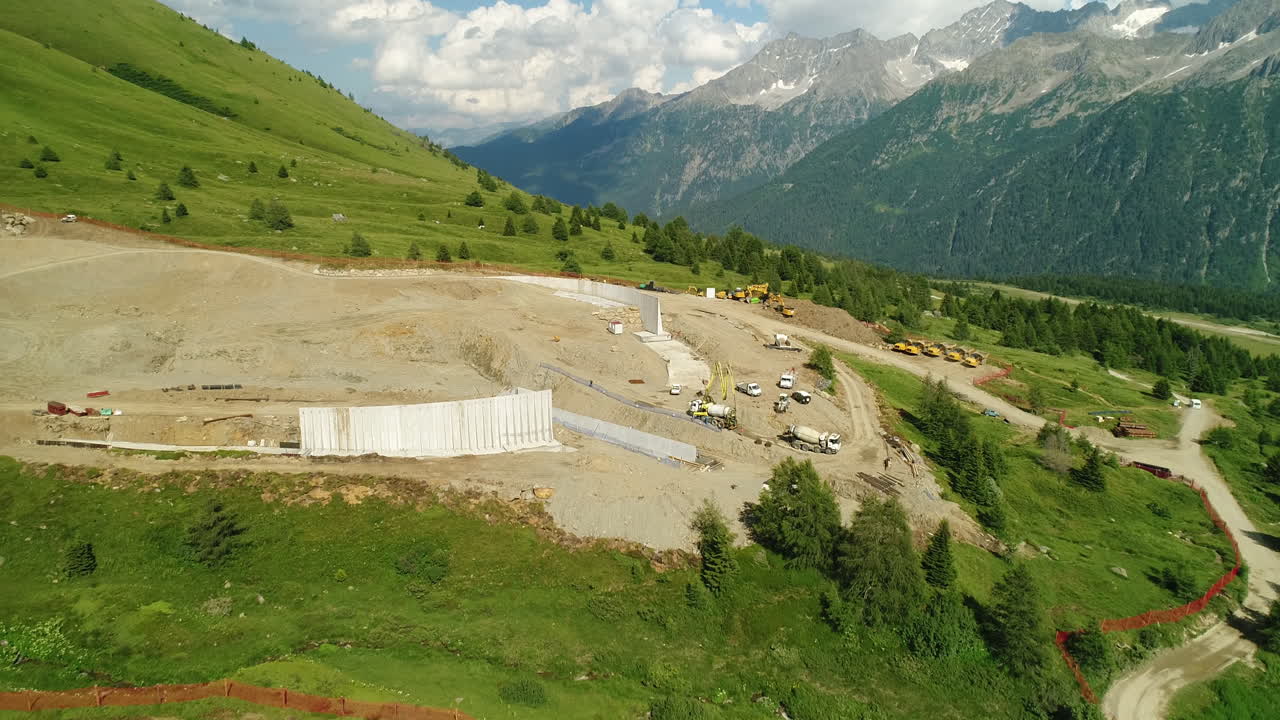 Ripresa aerea con drone dall'alto di un cantiere di costruzione di una diga nelle montagne alpine.