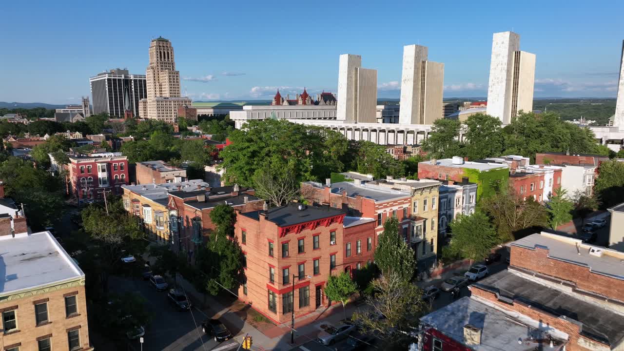 Low altitude Flight over roofs of brick houses and homes in Albany downtown. Sunset time. Modern buildings at Empire State plaza in distance